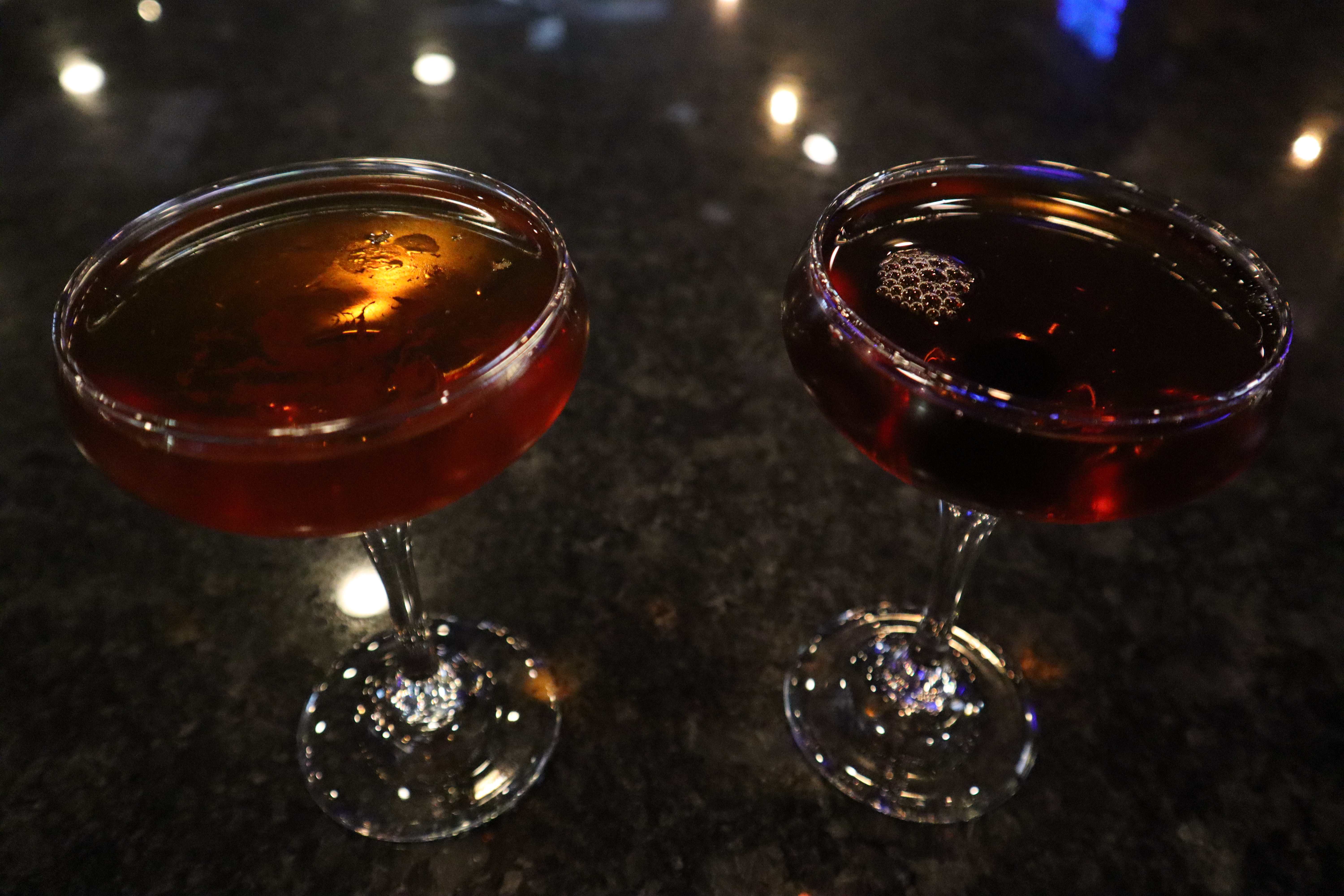 Two Manhattan cocktails on the dark reflective bar top